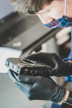 Technician in black gloves holding a professional video camera recorder outdoors.
