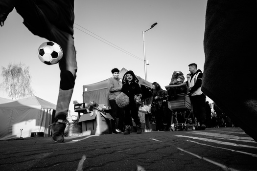 Soccer player's leg kicking a ball toward a group of people standing on a street.