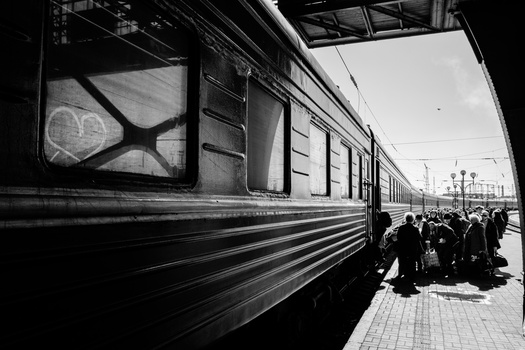 Black and white photograph of a passenger train car with passengers boarding on a platform.