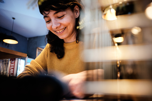 Woman in mustard sweater smiling while working at a desk with warm interior lighting.