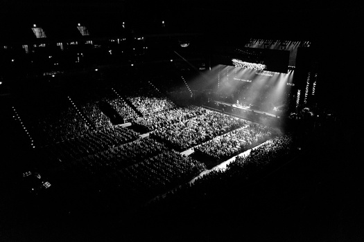 Aerial view of a large concert venue filled with thousands of attendees under dramatic stage lighting.