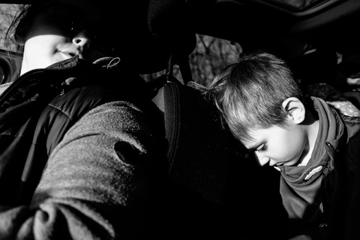 Young child sleeping in a car seat during daytime, captured in black and white photography.