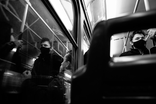 Passengers on public transportation viewed through windows in high-contrast black and white.
