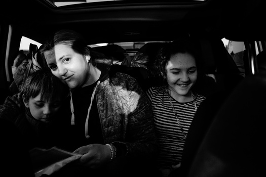 Three people seated in the back of a car, captured in black and white.