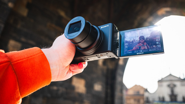 Hand holding Sony camcorder with extended articulating LCD screen displaying recorded footage.