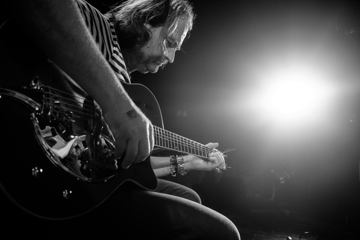 Musician playing electric guitar under dramatic stage lighting in black and white.