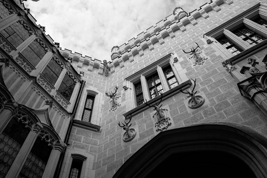 Upward view of a stone courtyard with arched entryway, windows, and mounted decorative elements on the walls.