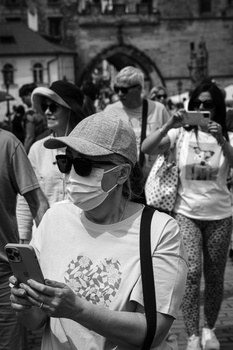 Black and white street photograph of people wearing masks and casual clothing gathered in an urban plaza.