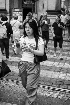Young woman in graphic t-shirt walking through crowded urban plaza, captured in black and white street photography.