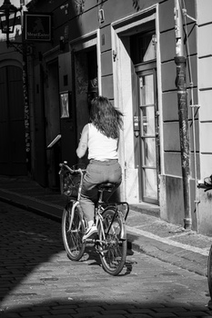 Woman riding a bicycle down a narrow urban alley in a black and white photograph.