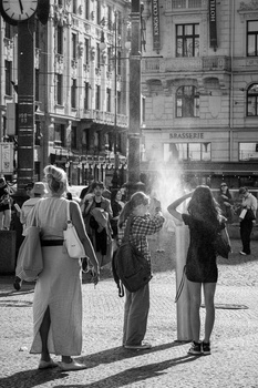Crowd of pedestrians gathered on a city street between historic buildings in bright sunlight.