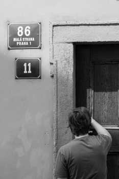 Person from behind reaching toward a dark wooden door on a weathered wall with street address plaques.
