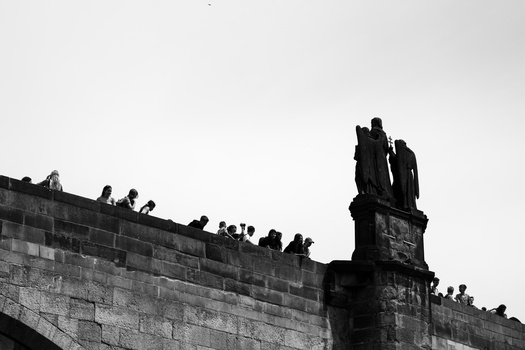 Silhouetted figures perched on a stone fortification wall and tower against an overcast sky.