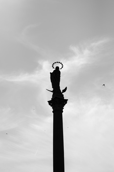 Silhouette of a tall ornamental column topped with a decorative crown finial against a cloudy sky.