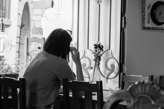 Person sitting by a window in black and white, hand raised to face in contemplative pose.