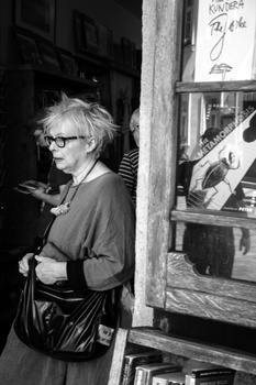 Woman wearing glasses and a jacket examining items in a storefront window display.