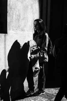 Woman in traditional dress standing against weathered wall with strong shadow cast by sunlight.