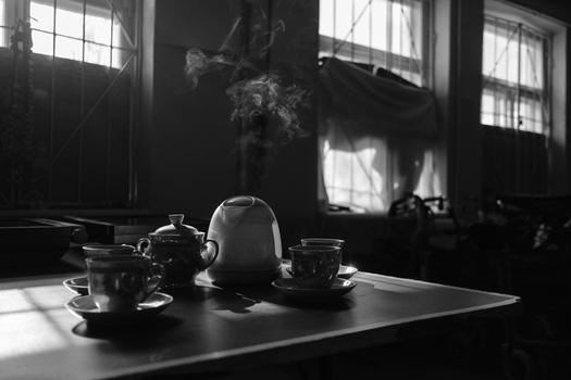 Steaming teapot and cups on a table with dramatic window light and dark interior.