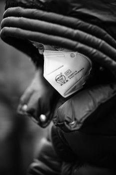 Gloved hands holding a white medical face mask in close-up, black and white photograph.