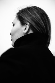 Profile view of a person with long dark hair wearing a black turtleneck against a white background.
