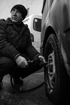 Man crouching beside a vehicle tire, adjusting or inspecting it in black and white.