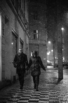 Two people walking toward the camera down a wet, patterned-stone European street at night.