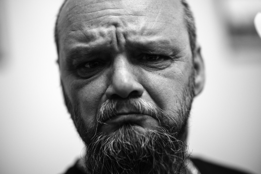 Black and white close-up portrait of a man with a full beard, looking downward with a contemplative expression.