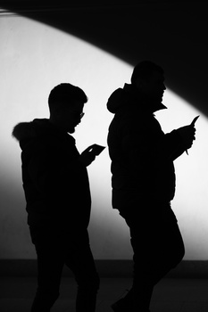 Two silhouetted figures standing against a bright backlit surface, engaged in conversation or interaction.