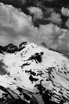 Snow-covered mountain peak with dramatic dark sky and white clouds above.