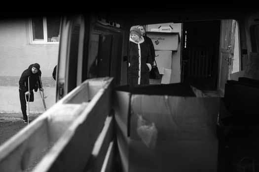 Two figures in a stark hallway with strong diagonal shadows cast across white walls and dark doorways.