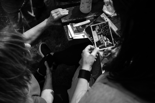 Multiple hands holding and examining printed photographs in black and white overhead view.