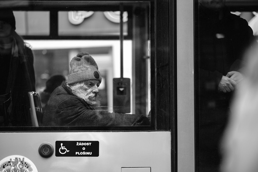 Man wearing a winter hat and glasses looking out from inside a public transit vehicle through the window.