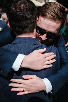 Two men in dark suits embrace at what appears to be a formal event, with one wearing sunglasses.