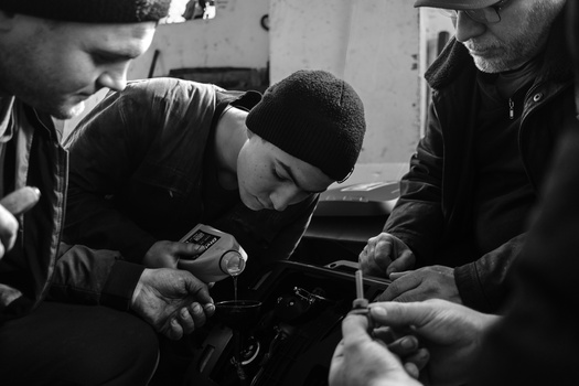 Multiple hands examining a vintage film camera in black and white.