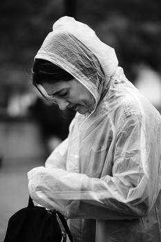 Person wearing a light-colored rain jacket with hood pulled up, looking downward in contemplative pose.