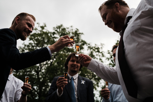 Four men in formal attire toasting with beer bottles outdoors.
