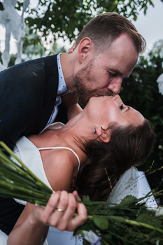 Groom dipping bride during a wedding kiss outdoors with green foliage in background.