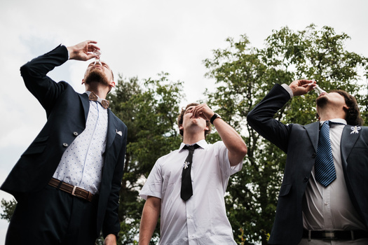 Four men in business casual attire shading their eyes while looking upward against a cloudy sky with trees.