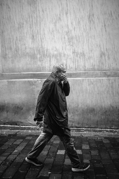 Person in dark jacket walking past weathered concrete wall in heavy rain.