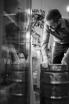 Man leaning over large wooden barrels in a cellar, examining contents in black and white.