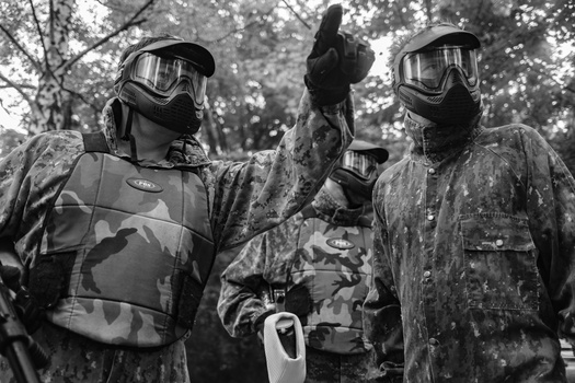Three paintball players in full protective gear and masks standing together outdoors.