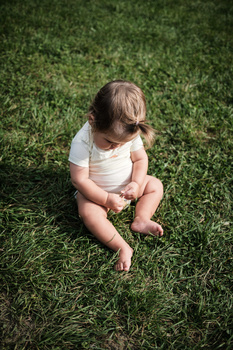 Toddler in white shirt sitting on grass looking downward.