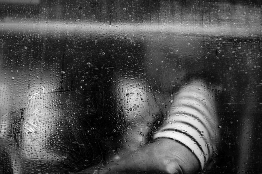 Hand pressed against rain-covered window glass, shot in black and white.
