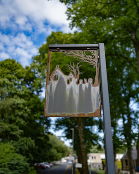 Street sign with illustration of white-robed figures in a field against trees and sky.