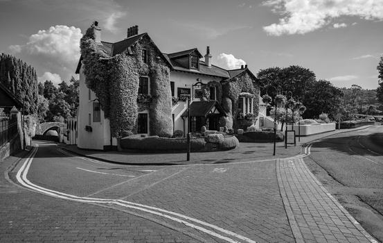 Ivy-covered corner building at a street intersection, photographed in black and white with dramatic clouds.