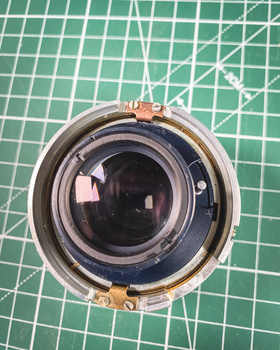 Disassembled camera lens element showing internal glass optics and metal housing on green cutting mat.