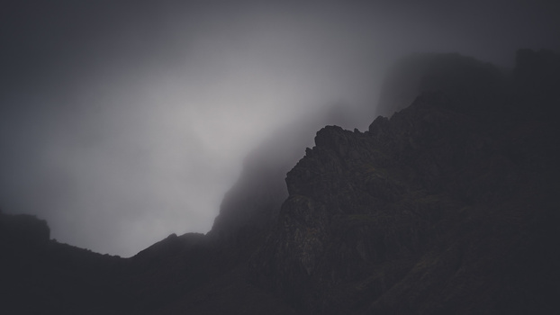 Dramatic silhouette of jagged mountain peaks shrouded in heavy mist and low clouds.