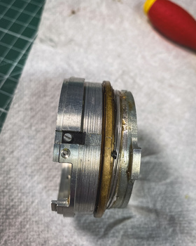 Disassembled camera lens components showing metal barrel sections and optical elements arranged on white paper.