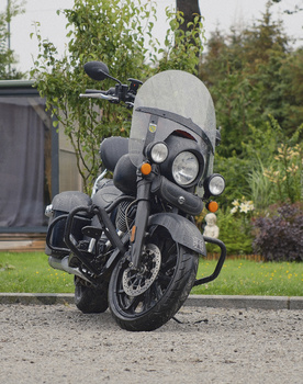 Classic motorcycle with windshield parked on gravel driveway in residential setting.