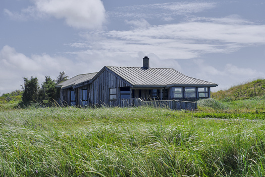 Modern dark blue residential building with metal roof set in expansive grassland under partly cloudy sky.
